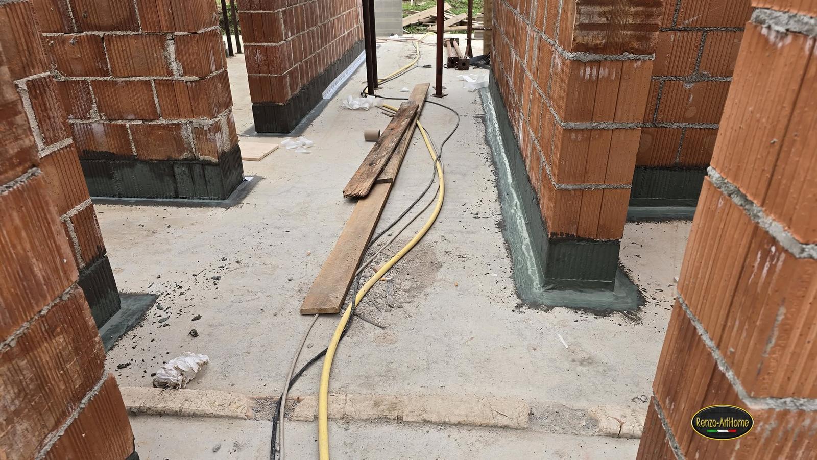 Base delle murature interne trattata con guaina cementizia e risvolto sul piano, in un cantiere al grezzo