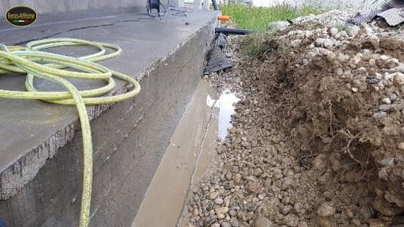 La trincea aperta lungo il cordolo, con l'acqua ancora sul fondo prima del trattamento