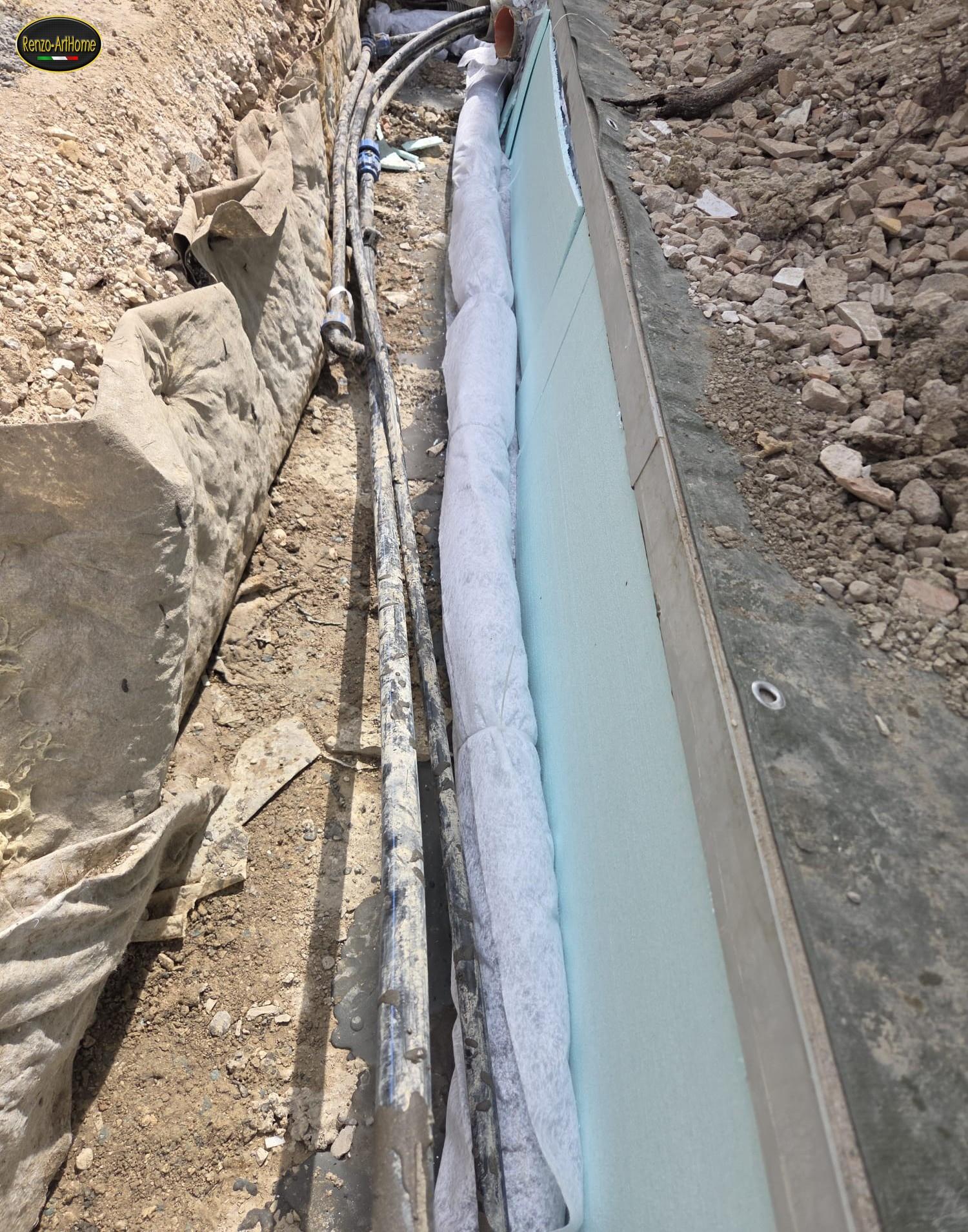 Tubo drenante rivestito di tessuto non tessuto appoggiato sul fondo dello scavo, lungo il muro impermeabilizzato e protetto da pannelli, con il tessuto steso contro la parete di terra e i cavi degli impianti che corrono a fianco