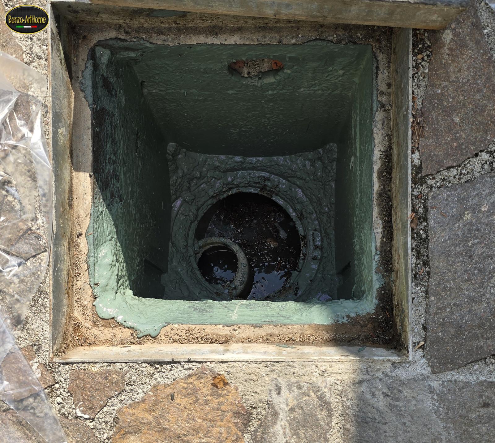 Pozzetto quadrato rivestito, con l'acqua ferma che copre la bocca di scarico e il tubo che entra sul fondo