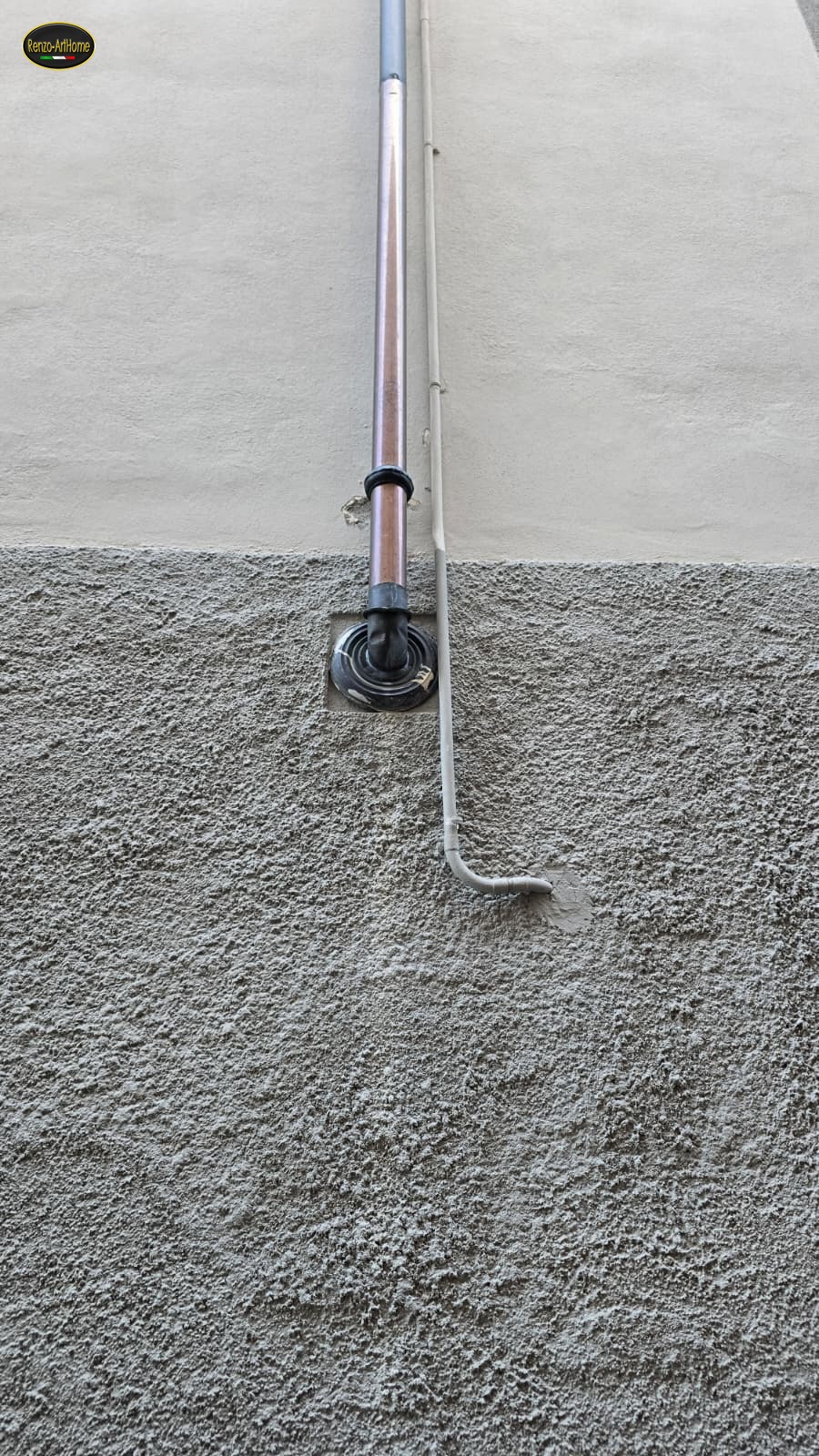 Particolare dell'innesto del pluviale dentro il muro: collare, raccordo nero e rosone nel riquadro dell'intonaco