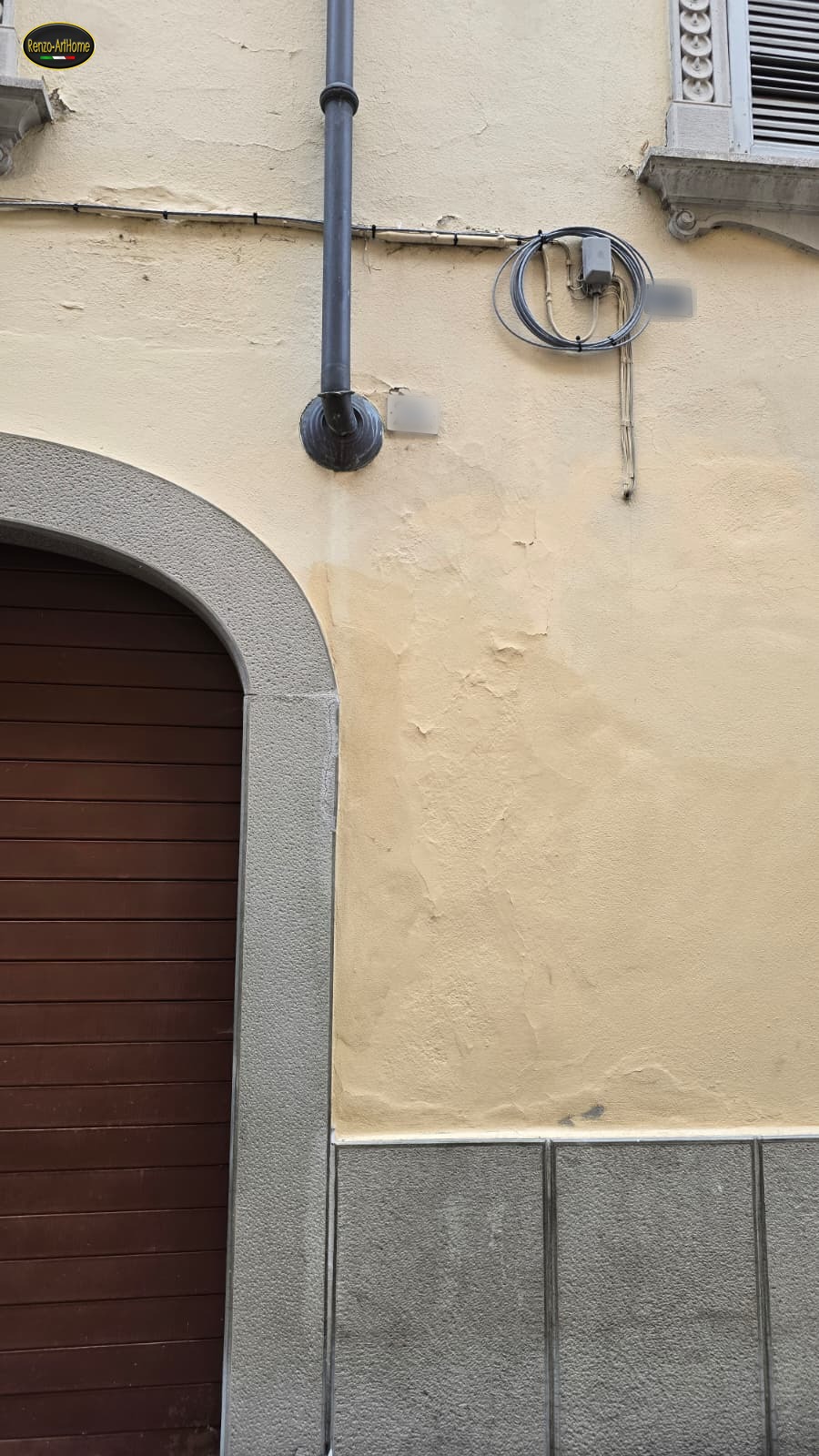 Innesto del pluviale dentro il muro all'altezza dell'arco di un portone, con l'intonaco rappezzato e di tono diverso sotto l'imbocco
