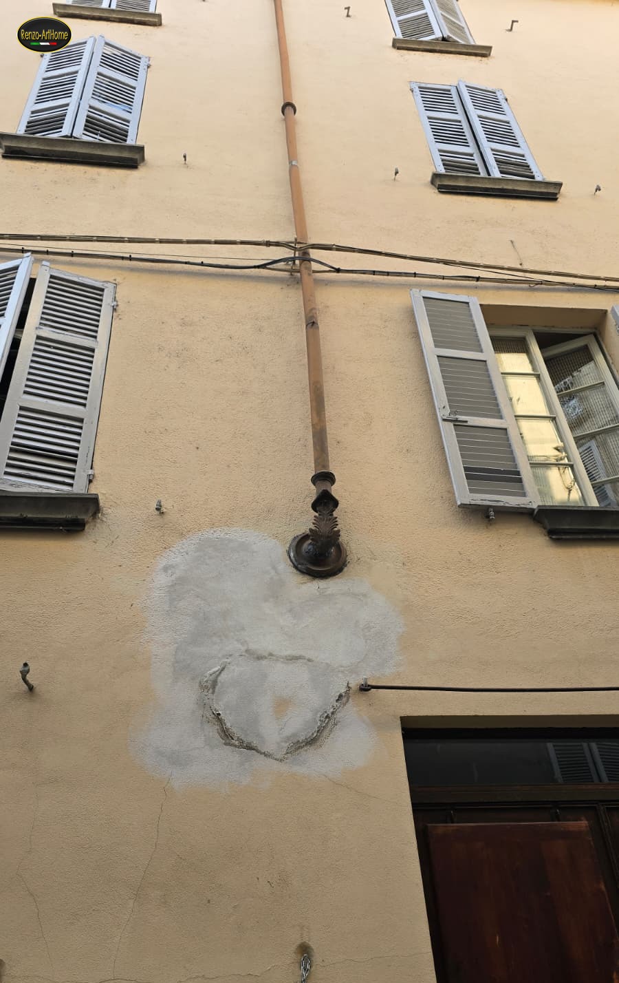 Pluviale con rosone decorato che entra nel muro, con una toppa grigia di intonaco rifatto subito sotto l'imbocco