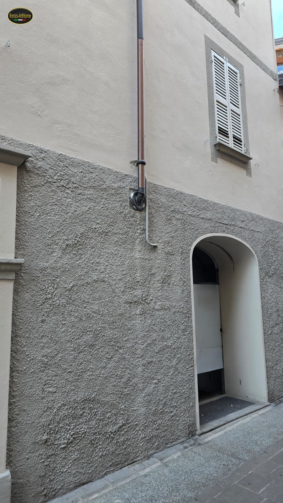 Pluviale in rame che entra nel muro dentro un riquadro, subito sotto il confine fra intonaco liscio e zoccolo ruvido